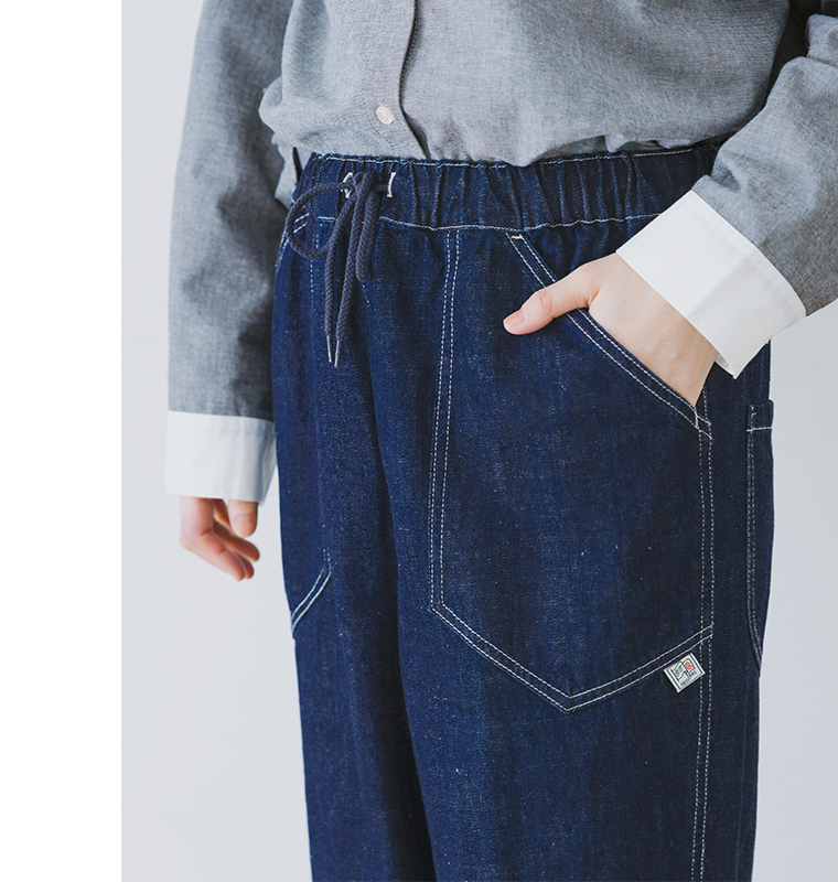 ネイビーデニムパンツのフロントポケットとドローストリングウエストのディテールアップ（白ステッチ・ブランドタグ付き）