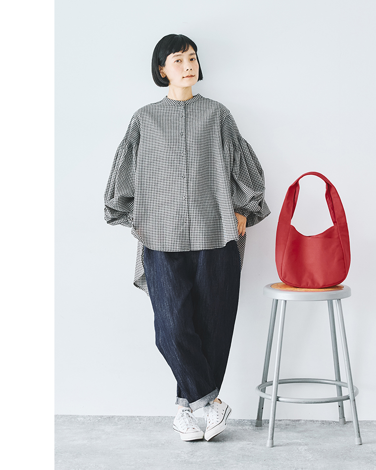 ボリューム袖の白黒チェックブラウスにロールアップデニムを合わせたカジュアルコーディネート（赤いバッグをスツールに置いたスタイリング）