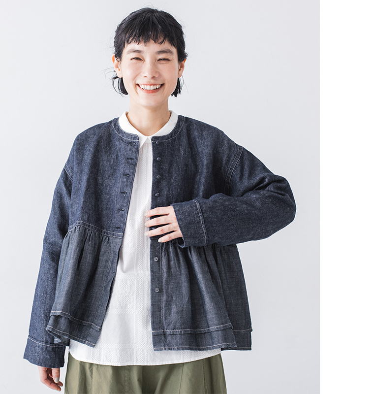 ペプラムデザインのデニムジャケットと白ブラウス、カーキパンツを合わせたカジュアルコーディネート（胸元に手を添えた笑顔のポートレート）