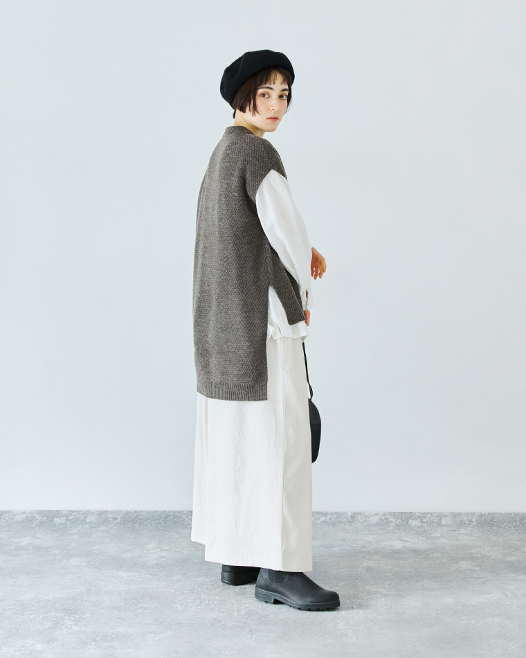 グレーのロングニットベストと白シャツ、白のパンツを合わせた全身コーディネート（黒ベレー帽と黒ブーツ）