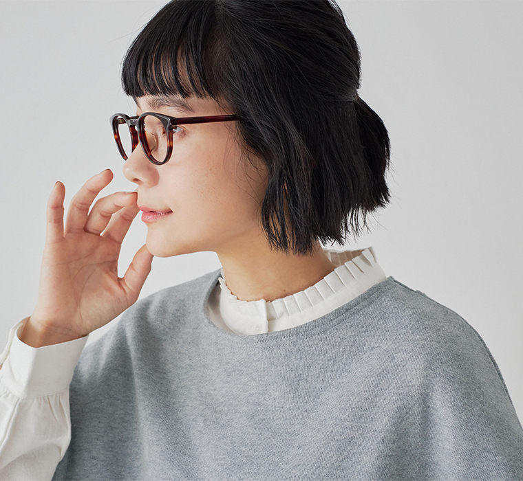 白のプリーツ襟ブラウスにグレーのベストを重ねた女性の横顔アップ（べっ甲柄メガネ）