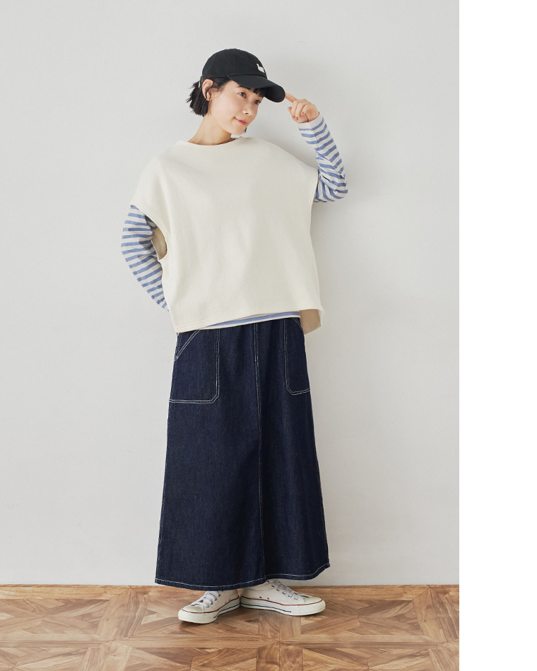 白のベストとブルーストライプシャツ、ロングデニムスカートを合わせたカジュアルコーディネート（キャップをかぶった女性）
