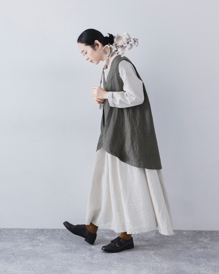 白のロングワンピースにチャコールのベストを重ねたコーディネート（ドライフラワーを顔元に持つ女性）
