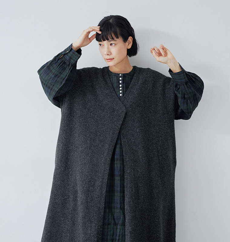  チャコールのロングベストとチェックワンピースを重ねたコーディネート（両手を顔の横に上げたポーズ）