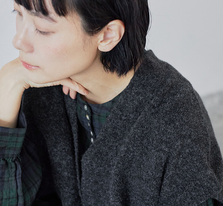 チャコールのベストとグリーン系チェックワンピースを重ねたコーディネート（顎に手を添えた女性のポートレート）