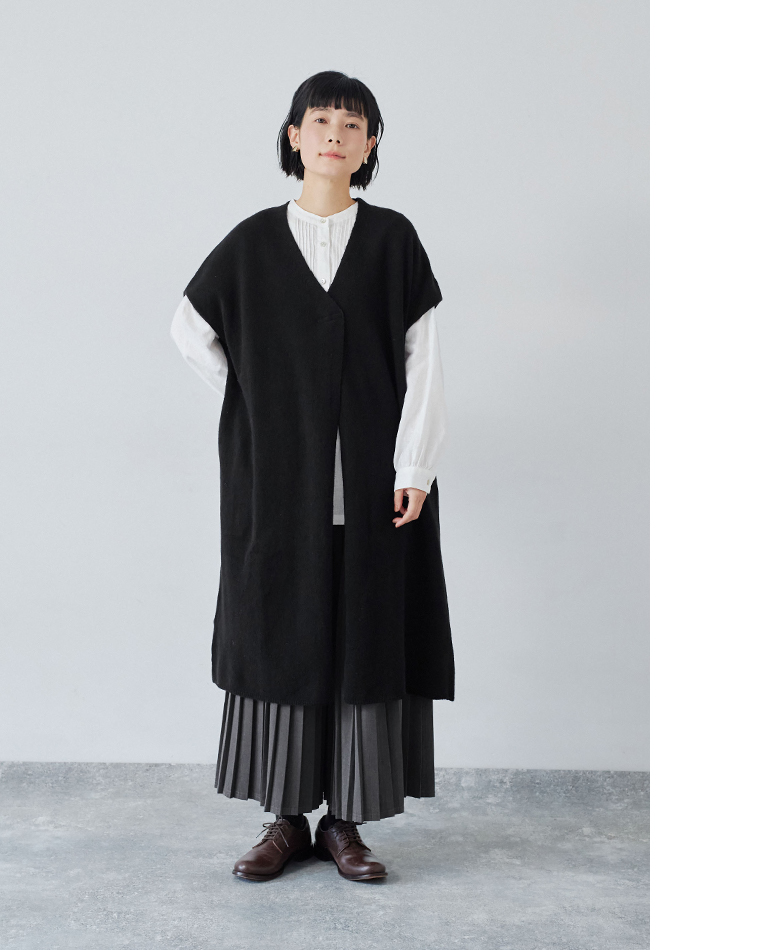 ブラックのロングベストと白のプリーツブラウス、グレーのプリーツスカートを合わせたコーディネート