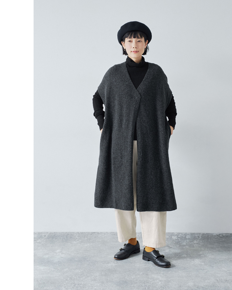 チャコールのロングベストと黒のタートルネック、クリーム色のパンツを合わせたコーディネート（ブラックベレー着用）