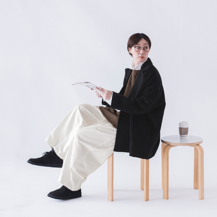 ブラックコートを着て椅子に座って振り返る女性モデル（全身）