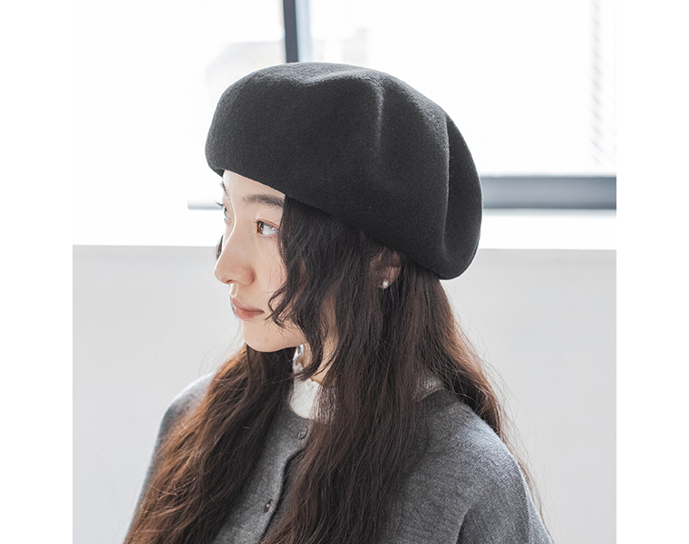 黒の八角ビッグベレー帽を横向きでかぶる女性。自然なドレープが見える着用シーン。