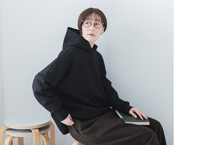 黒パーカーを着て椅子に座るカット（本を持つ横向き）