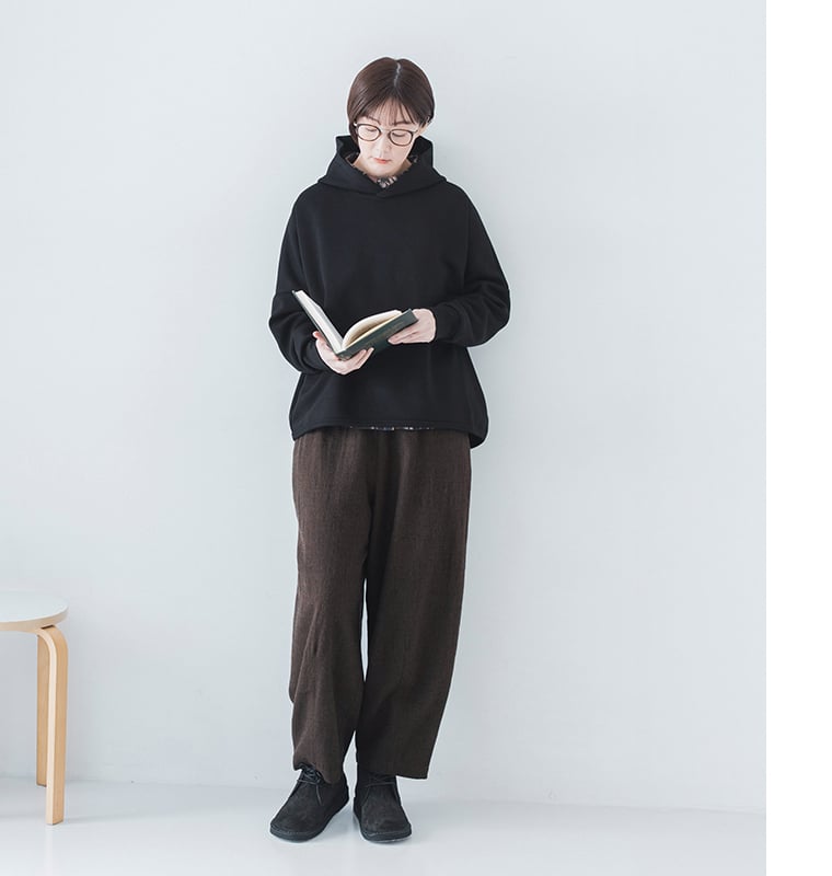 本を開いて読む立ち姿（黒パーカー・ブラウンワイドパンツ）