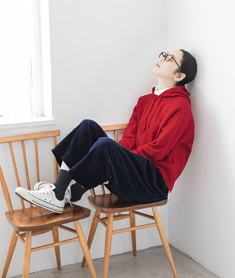 レッドのフーディーとコーデュロイパンツのリラックスコーディネート（椅子に横たわる姿）