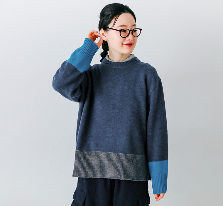 ラムウール配色切替セーター ネイビーを着用したモデルが床に座り手を頬に添えている