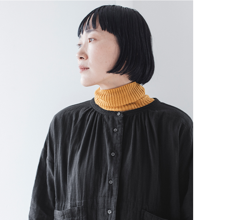マスタードのタートルネックと黒のギャザーブラウスを重ねた上半身のアップ