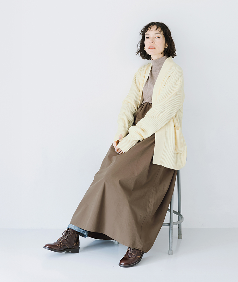 ニット×フハク ハイネックワンピース モカを着用しカーディガンを羽織って椅子に座ったモデルの全身