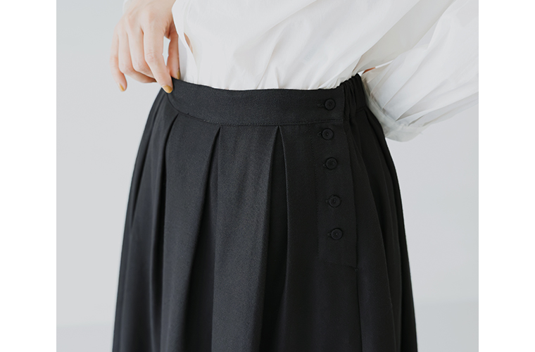 ウエストサイドにボタンを配したタックフレアスカート。後ろゴムでフィット感のある穿き心地。