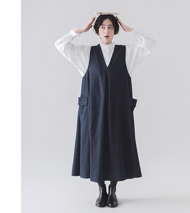 &yarn　コットンリネンデニム ジャンパースカート（ネイビー）を着用した女性モデルの全身カット。本を頭に乗せた遊び心あるポーズ