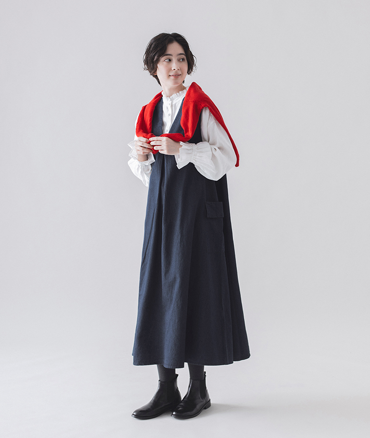 &yarn　コットンリネンデニム ジャンパースカート（ネイビー）を着用し、赤いニットを肩掛けした女性モデルの全身コーディネート