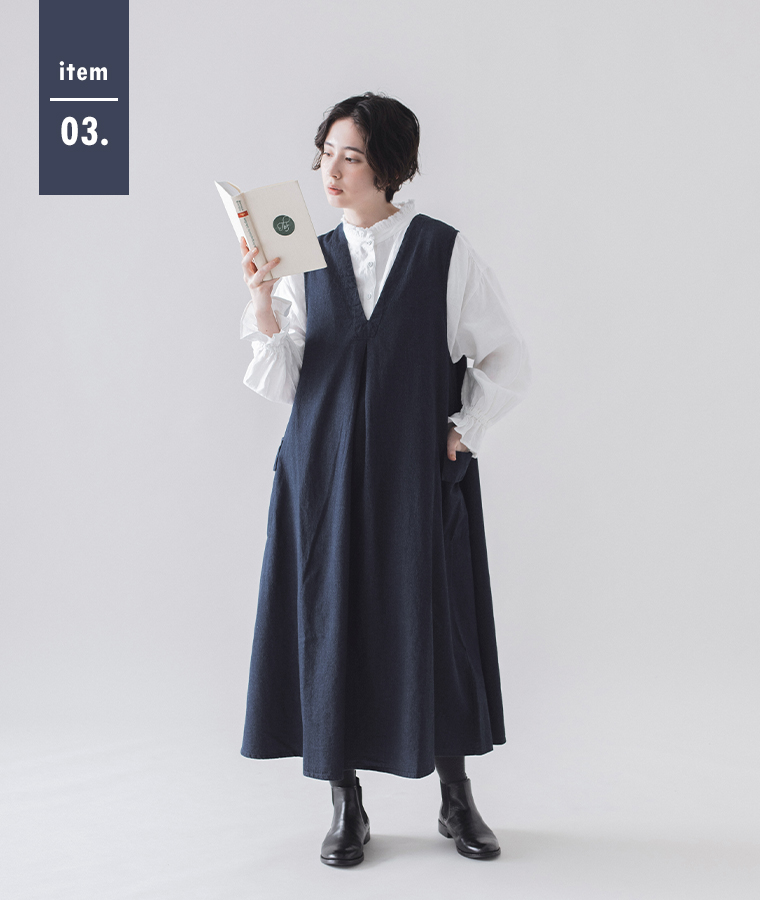 &yarn　コットンリネンデニム ジャンパースカート（ネイビー）を着用した女性モデルの全身コーディネート。白いフリルブラウスとブーツを合わせ、本を手に持っている様子