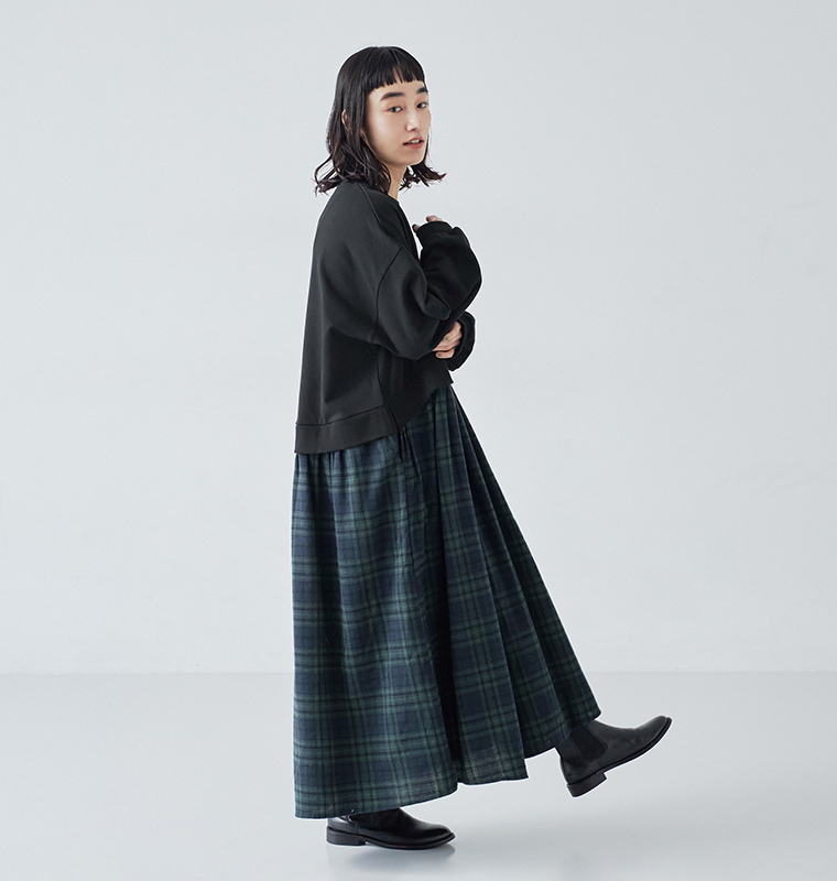 ブラックウォッチ柄の別注 裏毛切替ワンピースを横向きで着用した全身写真。チェック柄スカートのボリューム感が伝わるスタイル。