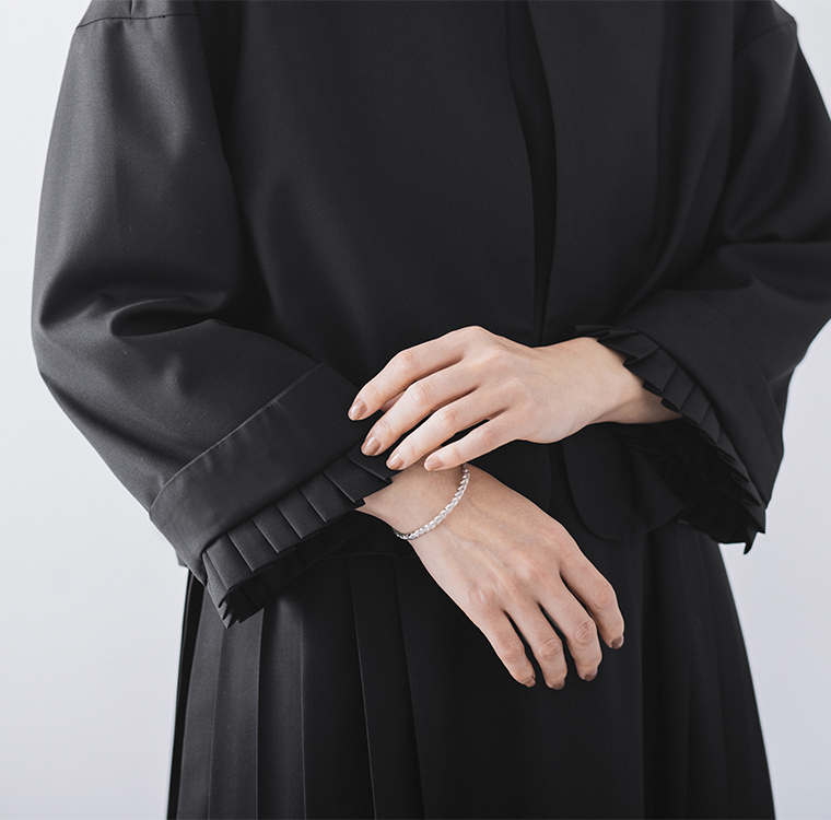 ブラックのジャケットの手元ディテール（ブレスレットとプリーツスカート）
