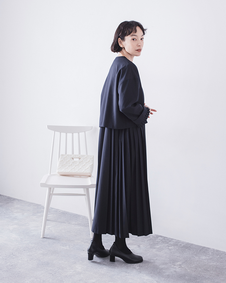 ネイビーのセットアップを着用した横姿（背景に白い椅子とバッグ）