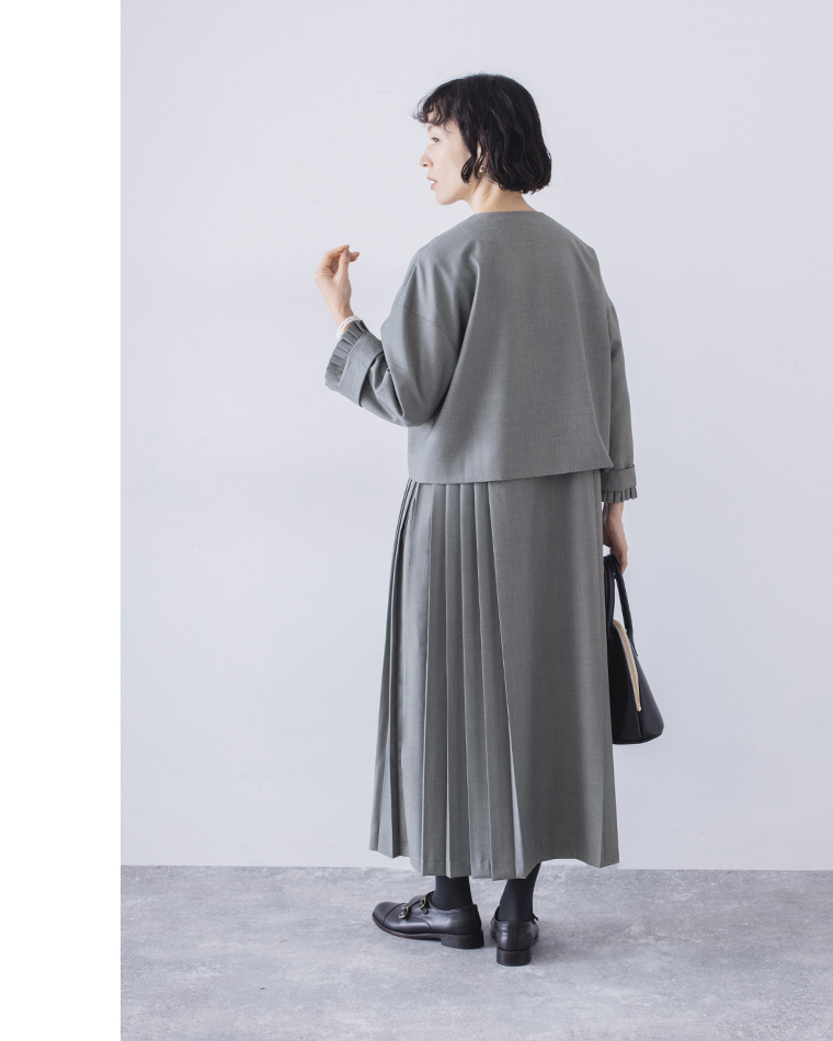 グレーのトップスとプリーツスカートのバックスタイル（バッグを持った自然なポーズ）