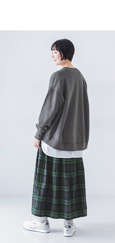 ピグメント裏毛斜め切り替えプルオーバー チャコールを着用し白のインナーとグリーン系チェック柄スカートを合わせたモデルの全身後ろ姿