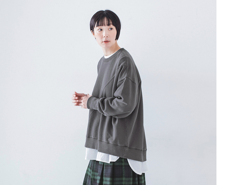 ピグメント裏毛斜め切り替えプルオーバー チャコールを着用し白のインナーとグリーン系チェック柄スカートを合わせたモデルの上半身横向き
