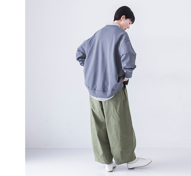 ピグメント裏毛斜め切り替えプルオーバー ブルーを着用したモデルの全身後ろ姿でカーキのワイドパンツと白のレースアップシューズを合わせたコーディネート