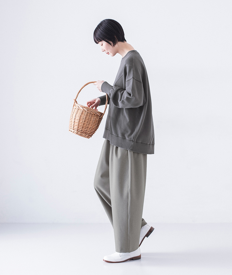 ピグメント裏毛斜め切り替えプルオーバー チャコールを着用したモデルの全身横向きでかごバッグを持ちワイドパンツと白のレースアップシューズを合わせたコーディネート
