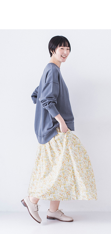ピグメント裏毛斜め切り替えプルオーバー ブルーを着用したモデルの全身横向き後ろ姿で小花柄スカートを合わせたコーディネート