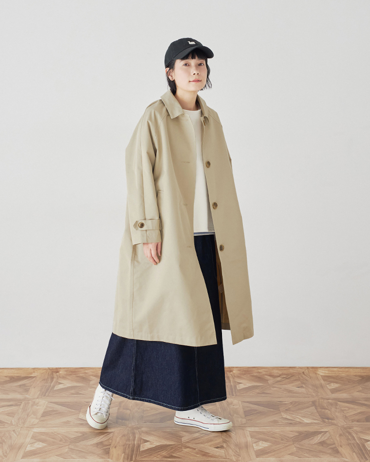 キナリの裏毛ベストの上にベージュのトレンチコートを羽織り、デニムスカートとキャップを合わせたスタイル