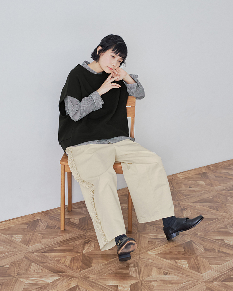 ブラックの裏毛ベストとチェックシャツ、フリルパンツを合わせたコーディネート（椅子に座り頬杖をついたポーズ）