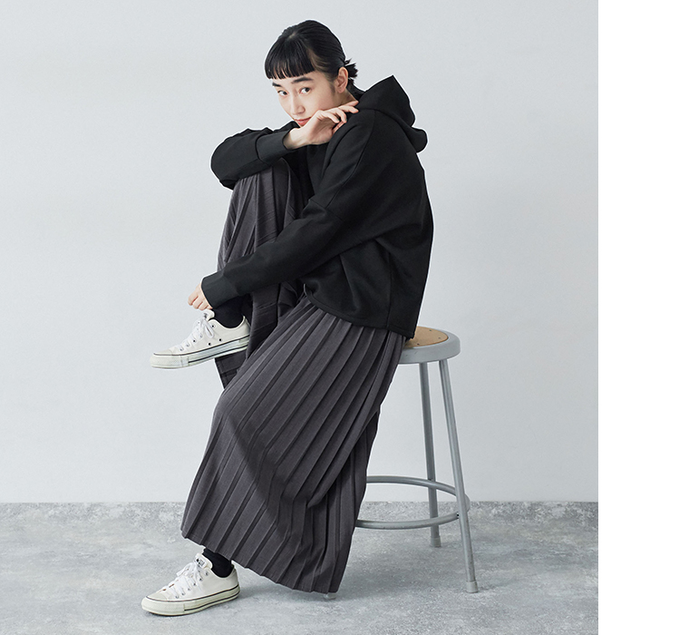 別注｜プリーツパンツのチャコールを着用したモデルがスツールに座っている