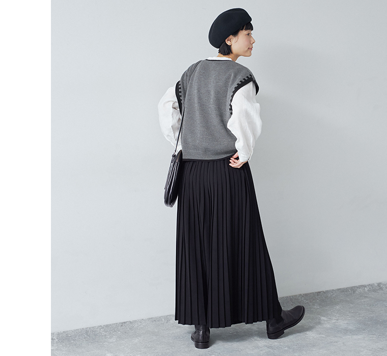 別注｜プリーツパンツ ブラックを着用したモデルを後ろから写しておりグレーのベストと黒いショルダーバッグが見えている