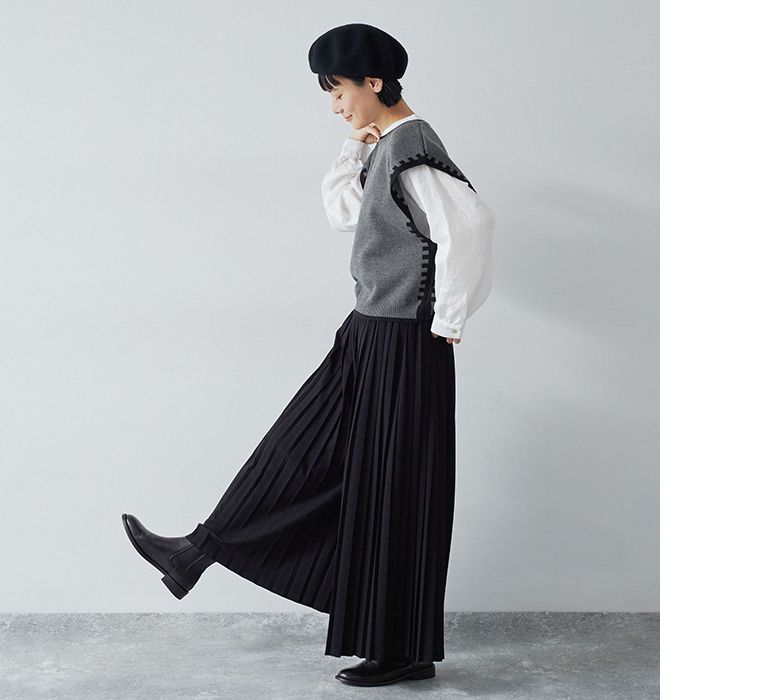 別注｜プリーツパンツ ブラックを着用したモデルが片足を上げてプリーツの動きを見せている