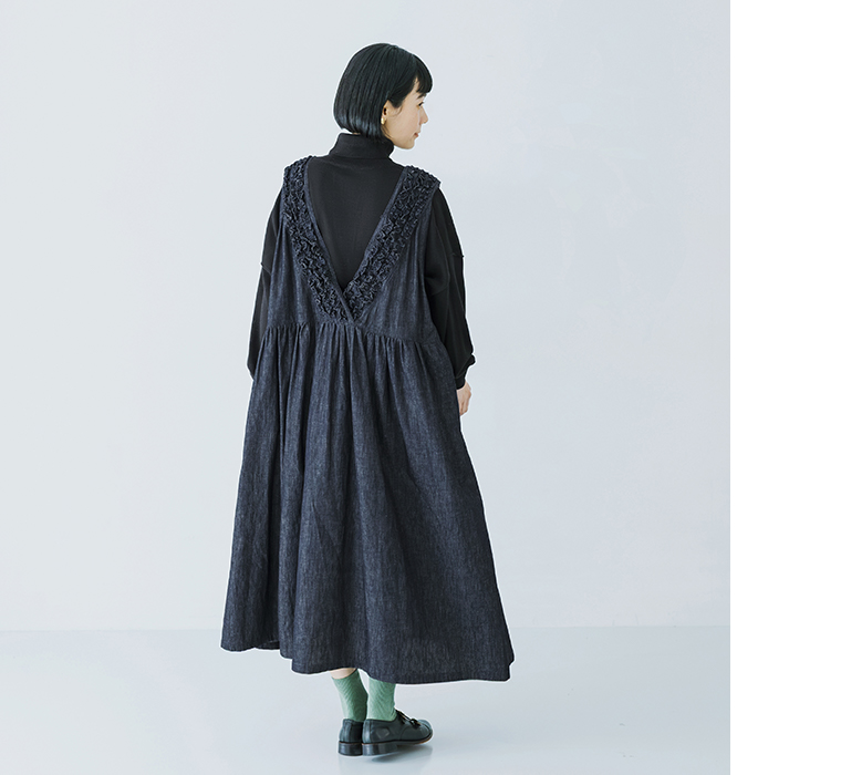コットンリネンループ染めインディゴ前後フリル使い2wayノースリーブワンピースのインディゴを黒のタートルネックの上に重ねて後ろ向きに立ち背中側のV字フリルとギャザーの入ったスカート部分が見える状態