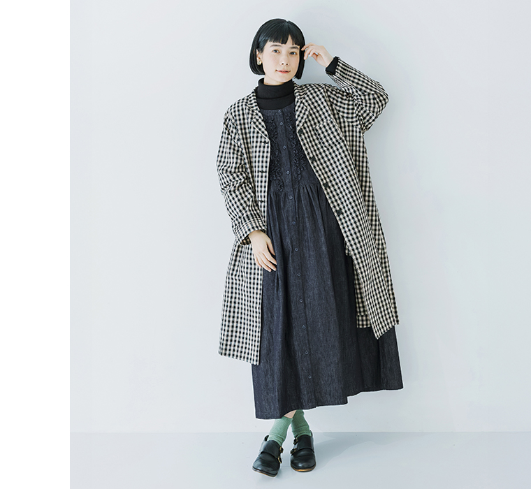 コットンリネンループ染めインディゴ前後フリル使い2wayノースリーブワンピースのインディゴを黒のタートルネックの上に重ねてチェック柄のコートを羽織り立っている全身コーディネート