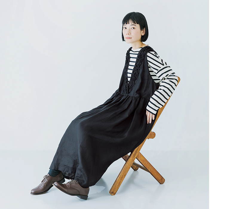 14番手洗いざらしリネン無地前後フリル使い2wayノースリーブワンピースのブラックを着用したモデルが椅子に座っている