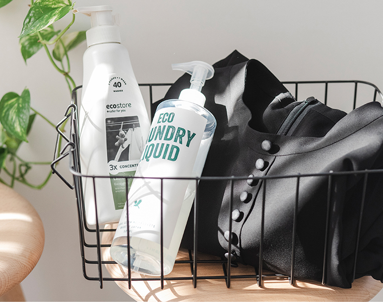 黒のボタン付きワンピースと洗濯用洗剤をワイヤーバスケットに入れたイメージカット