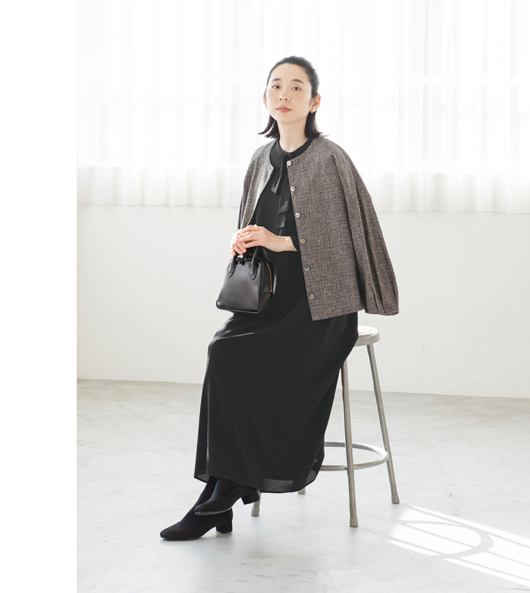 黒のボウタイ付きワンピースにジャケットを羽織り椅子に座ったコーディネート