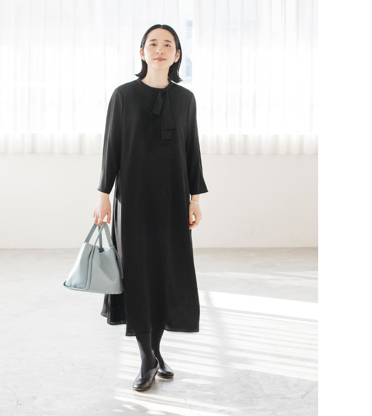 黒のボウタイ付きワンピースを着た人物が水色のバッグを持って立つコーディネート