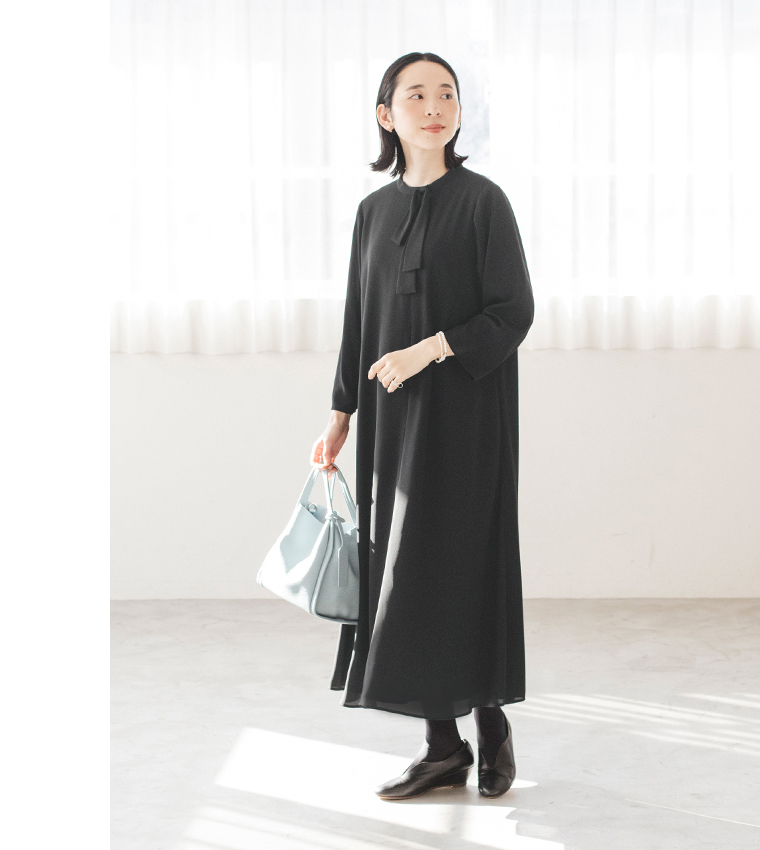 黒のボウタイ付きワンピースを着た人物が水色のバッグを持って立つ斜め前のコーディネート