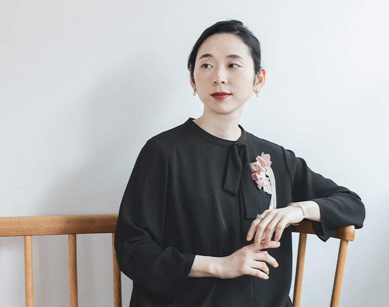 黒のボタンフレアワンピースとクラッチバッグ、パールネックレス、花を並べたフラットレイ