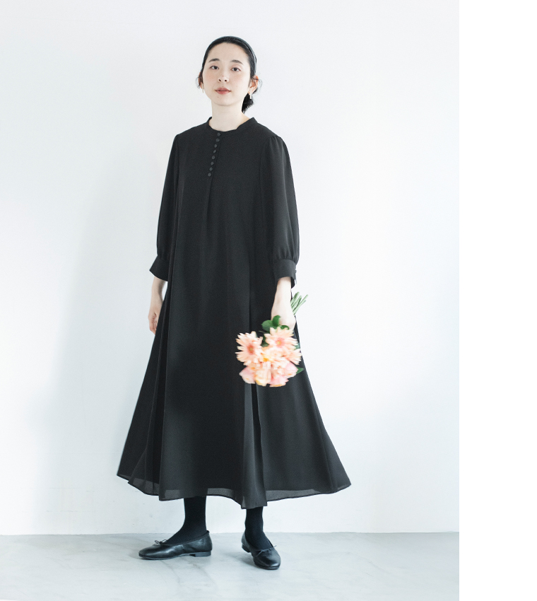 黒のボタン付きワンピースを着た人物が花束を持って立つ正面コーディネート