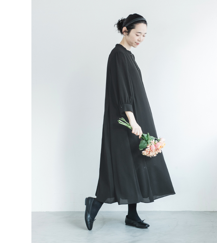 黒のボタン付きワンピースを着た人物が花束を持って立つ正面コーディネート