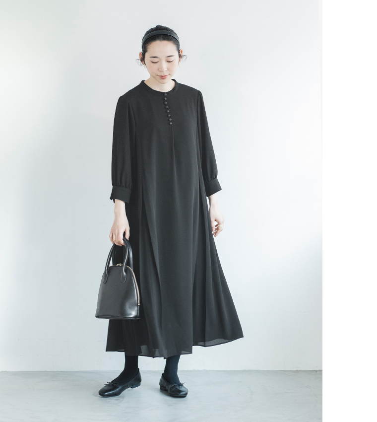 黒のボタン付きワンピースを着た人物が黒のバッグを持って立つ正面コーディネート