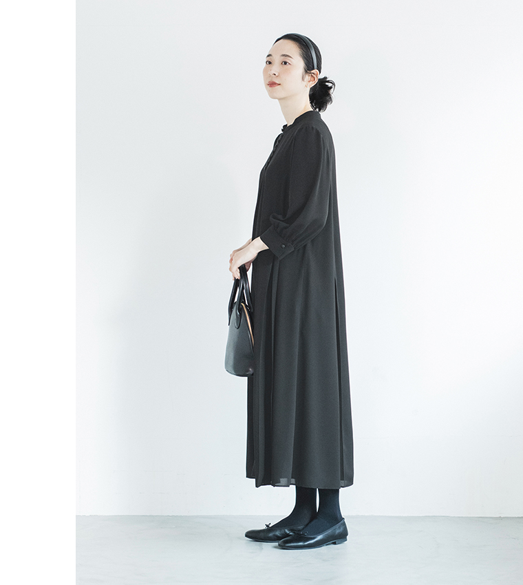 黒のボタン付きワンピースを着た人物が黒のバッグを持って立つ横向きのコーディネート