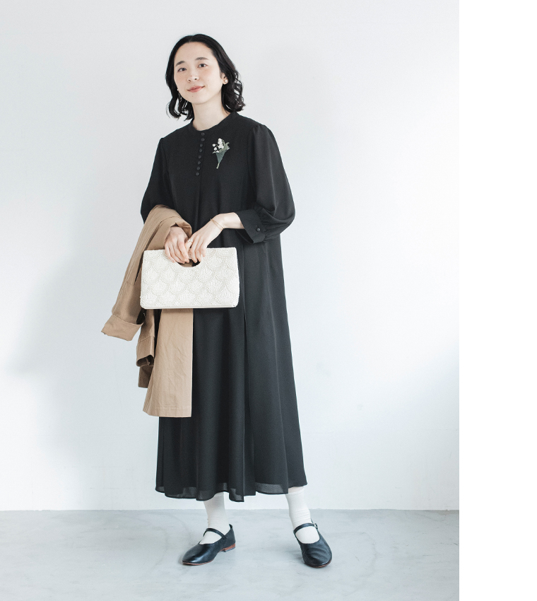 黒のボタン付きワンピースに花のコサージュをつけた人物がコートとバッグを持つコーディネート